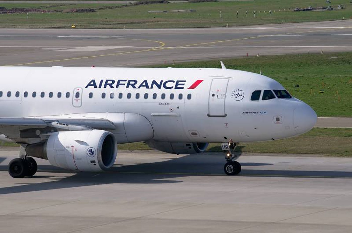 Un Airbus blanc de la compagnie Air France roule sur une piste d'aéroport bordée d'herbe.