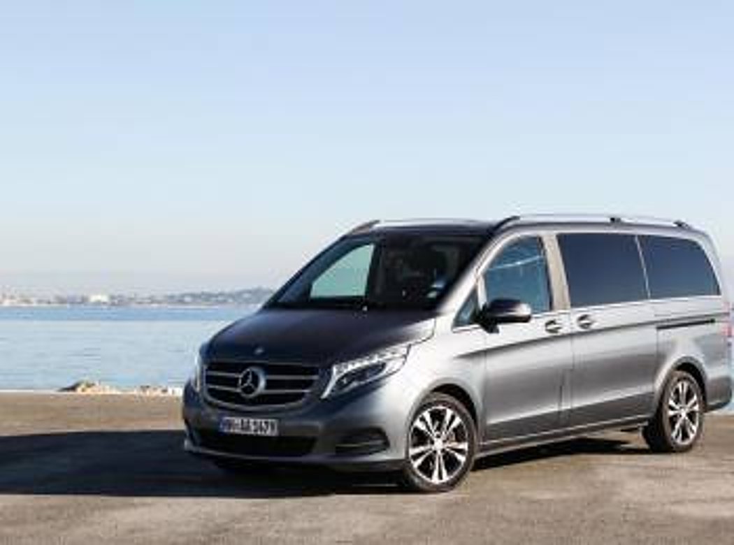 Un monospace Mercedes gris métallisé est garé sur un quai en bord de mer, sous un ciel dégagé.