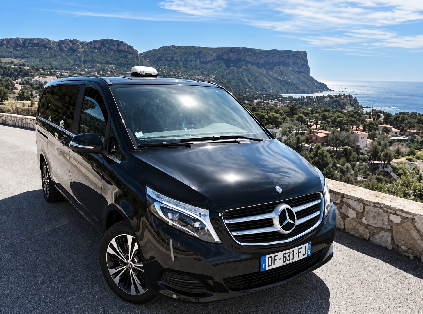 Van Mercedes noir arrêté sur une route en corniche, avec les falaises de Cassis et la mer derrière.
