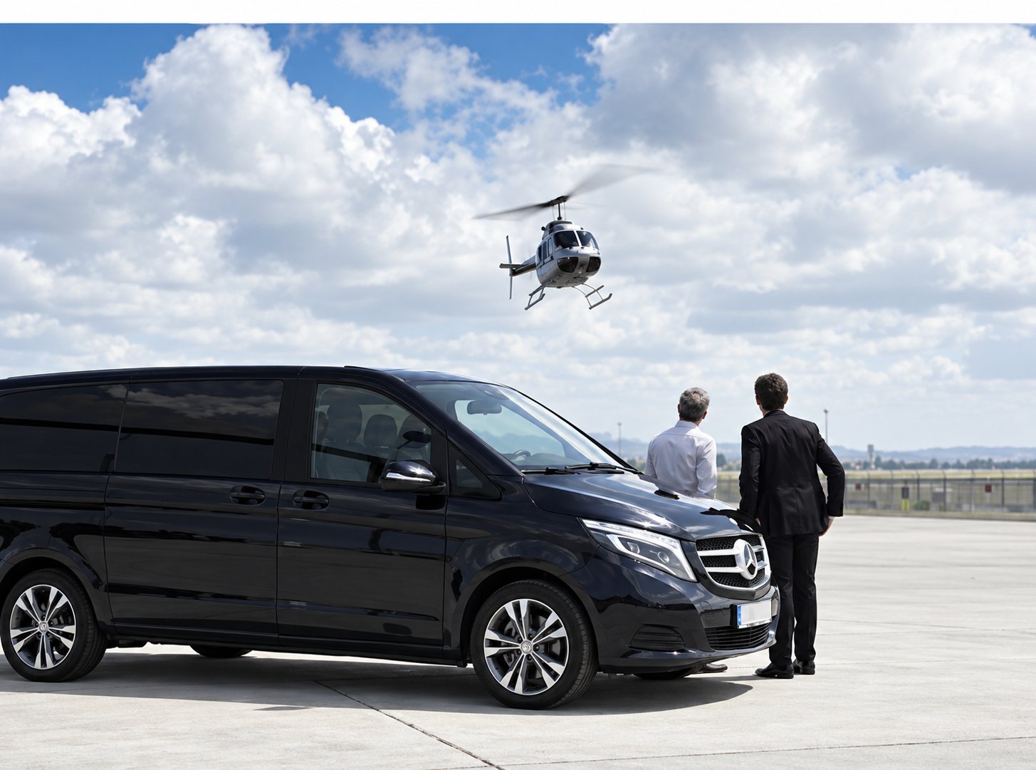 Un van noir de type Mercedes est garé sur une piste tandis que deux hommes en costume regardent un hélicoptère voler dans un ciel nuageux.
